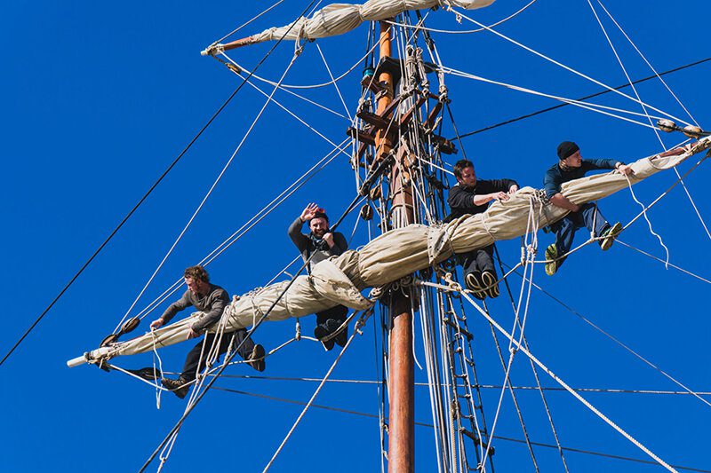 sailors work with sails at a height on a traditional sailboat in the sea